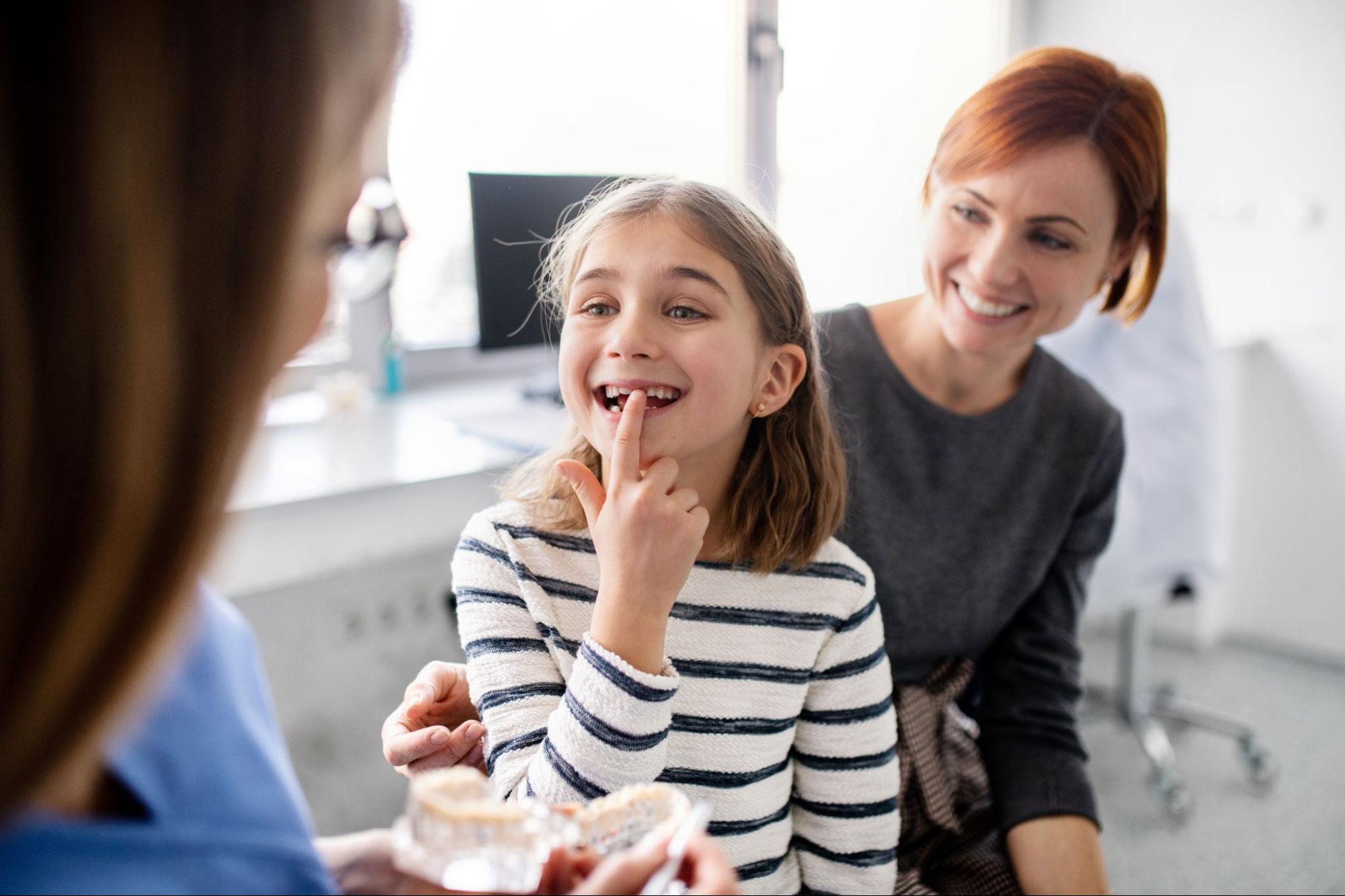 orthodontist springfield il-001 Young girl smiling and pointing at her teeth during an orthodontic consultation, with a parent and orthodontist present, highlighting personalized care at Bankhead Orthodontic Specialists in Springfield, IL.